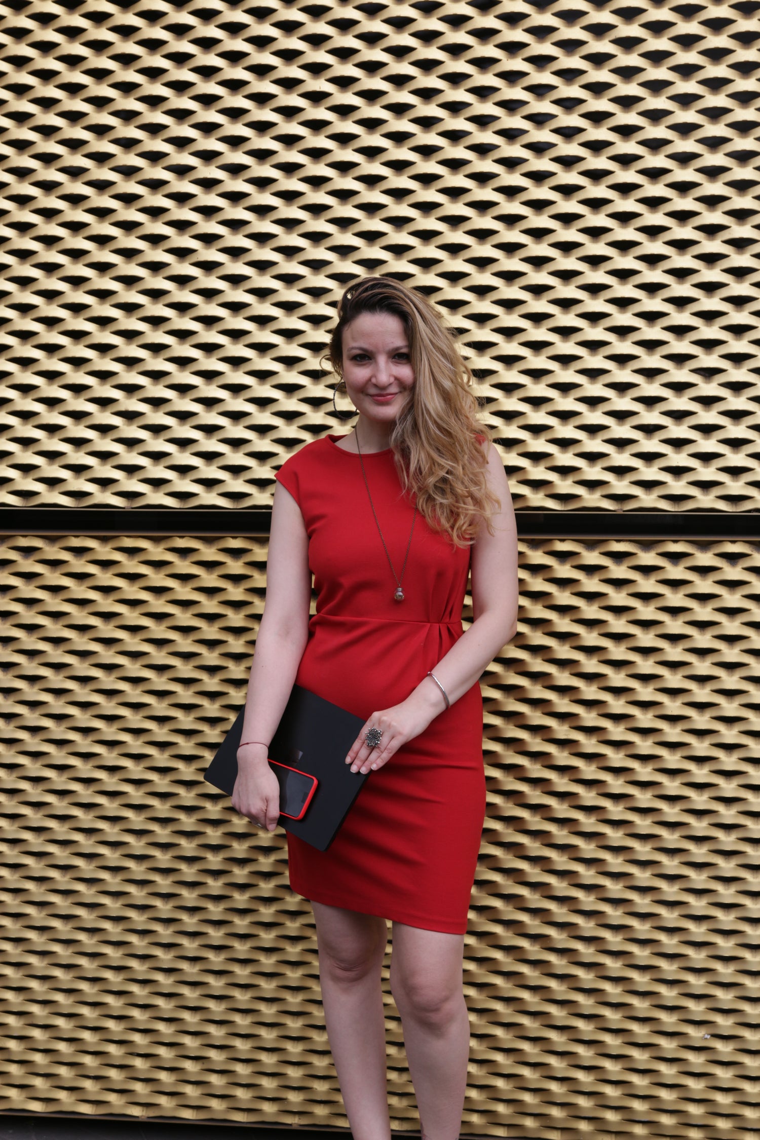 Ioana wearing a red dress against a gold background holding her laptop and phone
