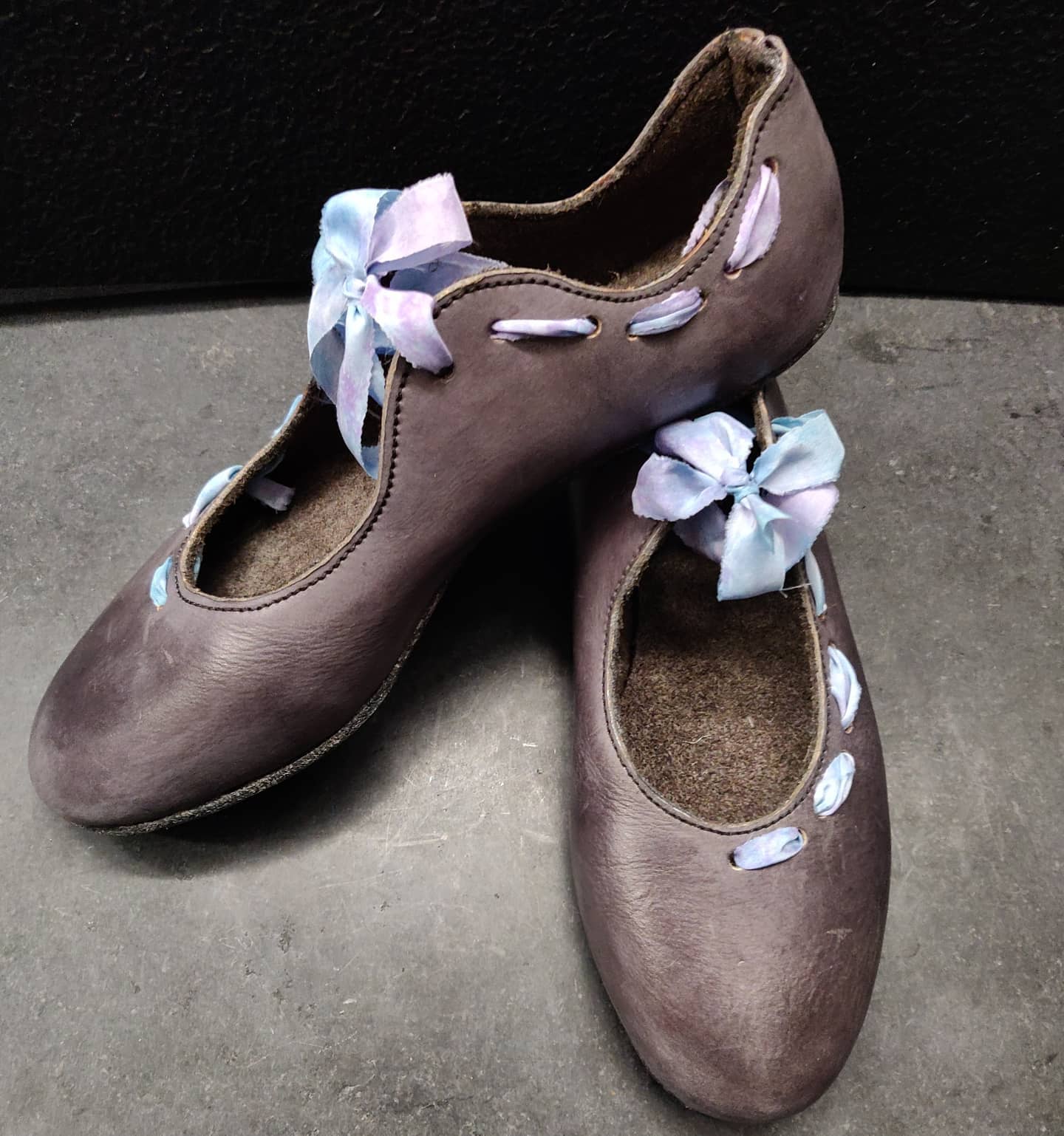 Pair of grey leather flats resembling a ballerina shoe shape. They tie at the front in a bow and the ribbon is asymmetric on each side of the shoe - front chain for the outside and back chain for the inner. The ribbon is hand dyed silk in soft blues and purples.  