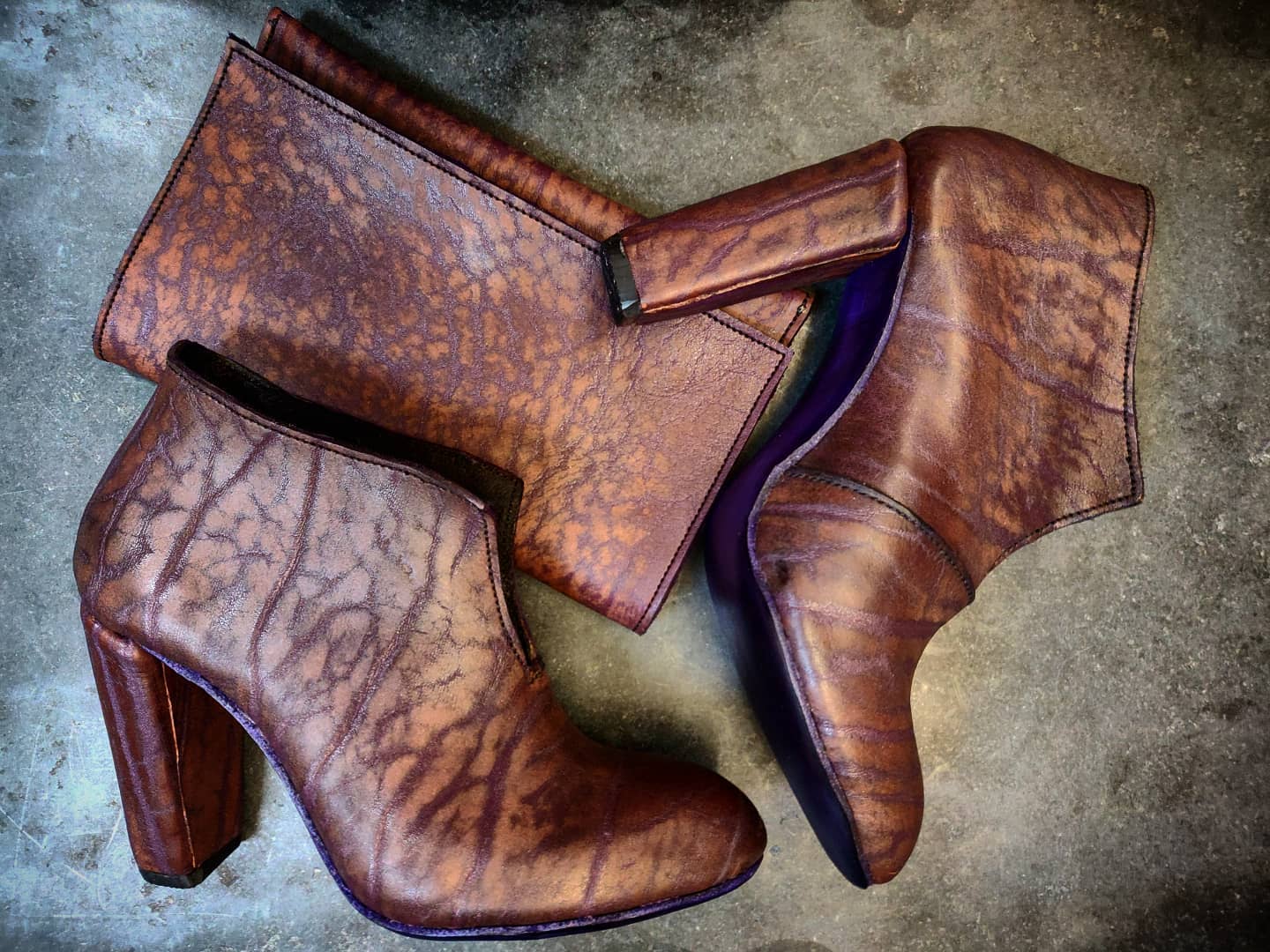Lateral view of the shoes, against a grey background and next to a pouch in the same leather. 