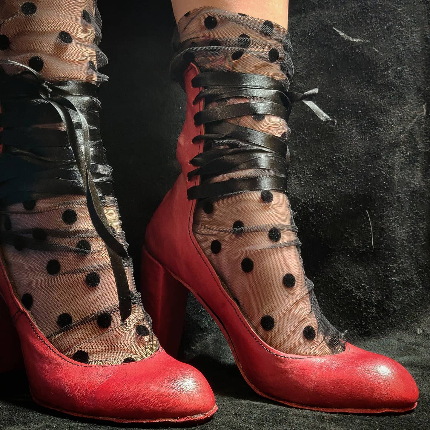 Red pumps with a 10cm block heel and a back panel going up on the back of the leg for aprox 15 cm high and held together on the leg with black silk lacing. They are also adorn and complemented by a tule sock with black dots 