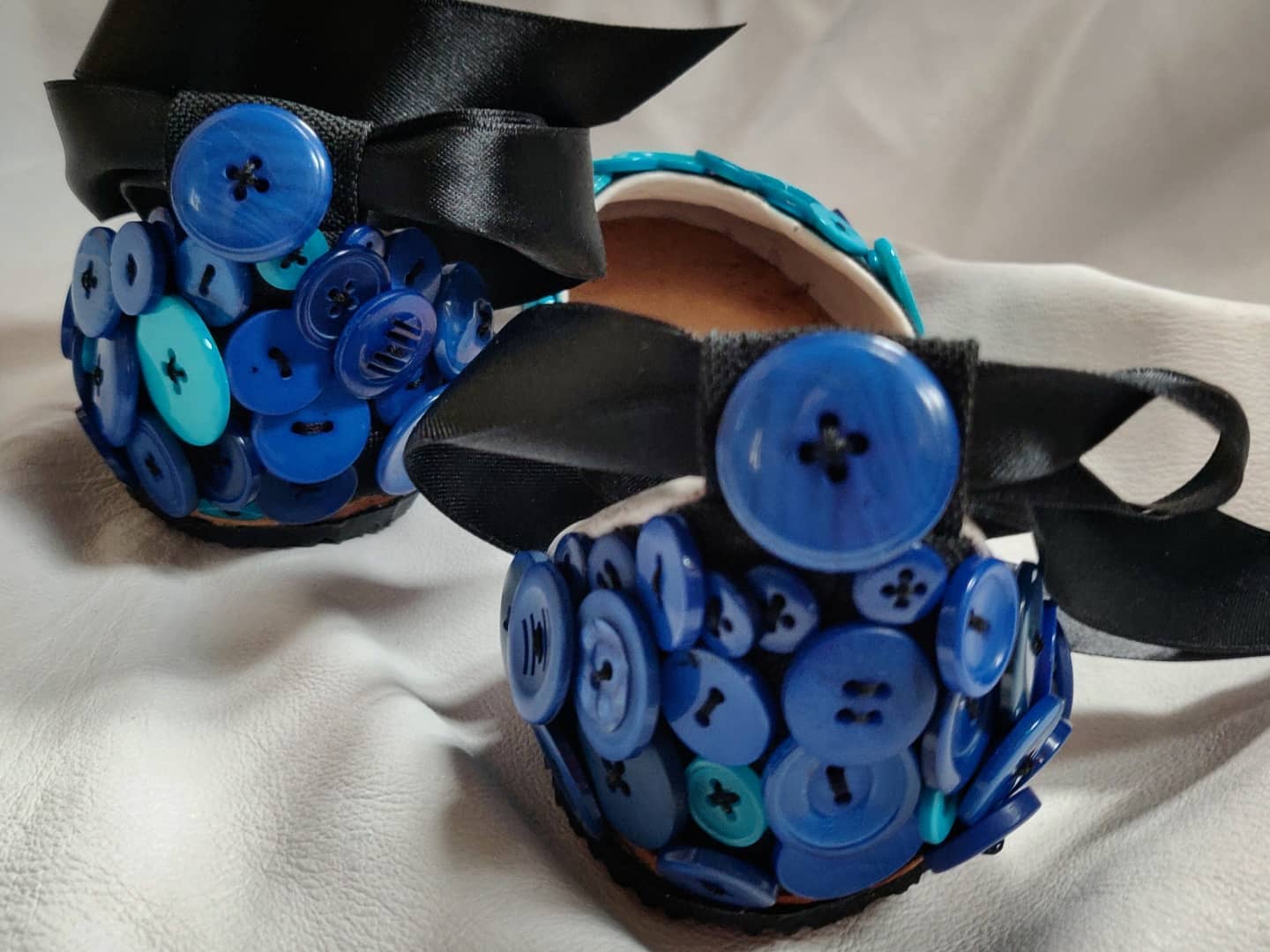 Heel area focus with blue buttons of various sizes covering the heel and with a strap around the ankle. These shoes can be worn up and down, depending on the attire. They are meant for sunny summer weather due to the fact they are more like a sandal