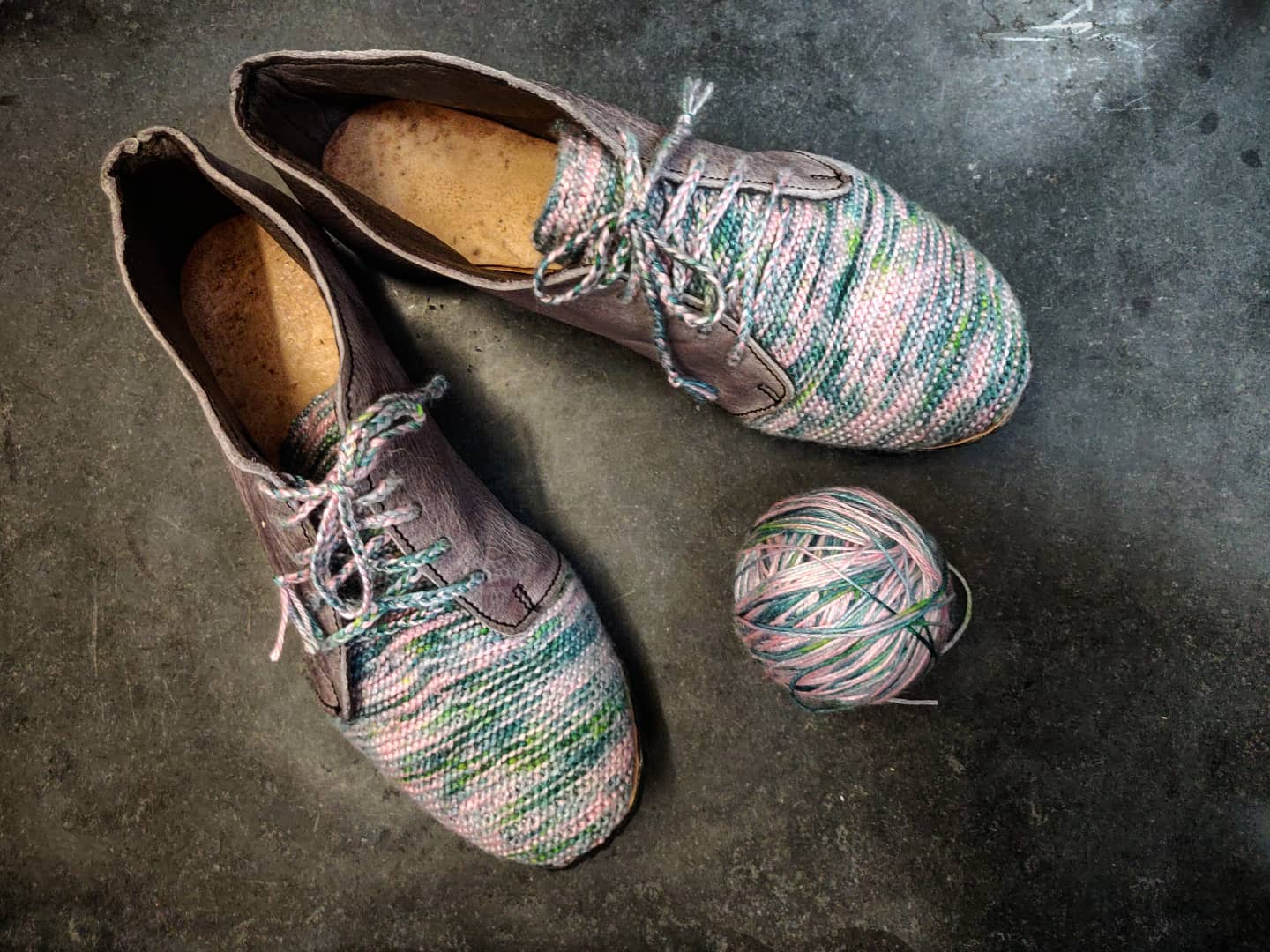 Pair of grey leather and knit sneakers next to a ball of yawn from the same wool thread. The knit bit is on the vamp and has shades of pink and green, with matching laces. The back and lateral panels are from purple grey leather