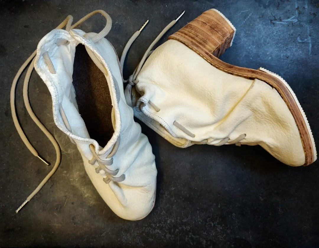 Lateral view of the shoe showing the natural leather sole in contrast with white rubber over soling. 