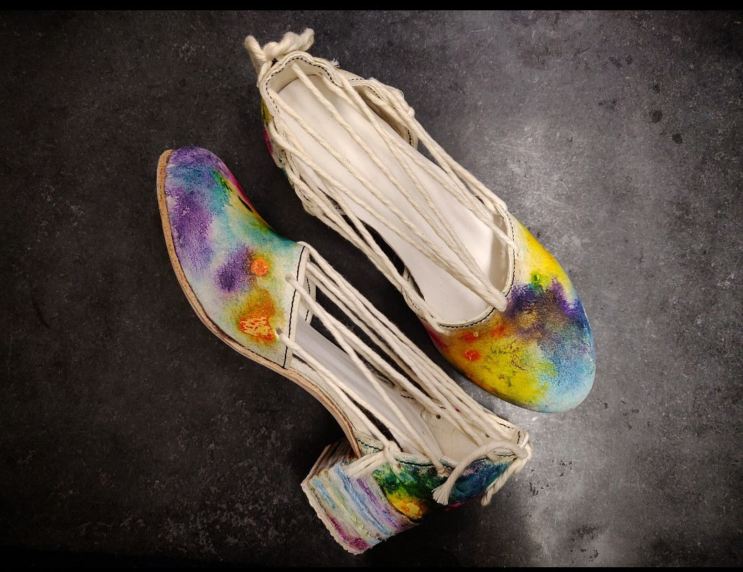 Shoes with a 5 cm heel comprised of two different sections. The front bit is similar to a slipper, while the back arches around the heel areas. They are brought together with soft macramé string which run across from back to forth creating a rope life feel to them. The leather sections as well as the 5 cm heel are painted with French shellac inks in an abstract color way pattern  