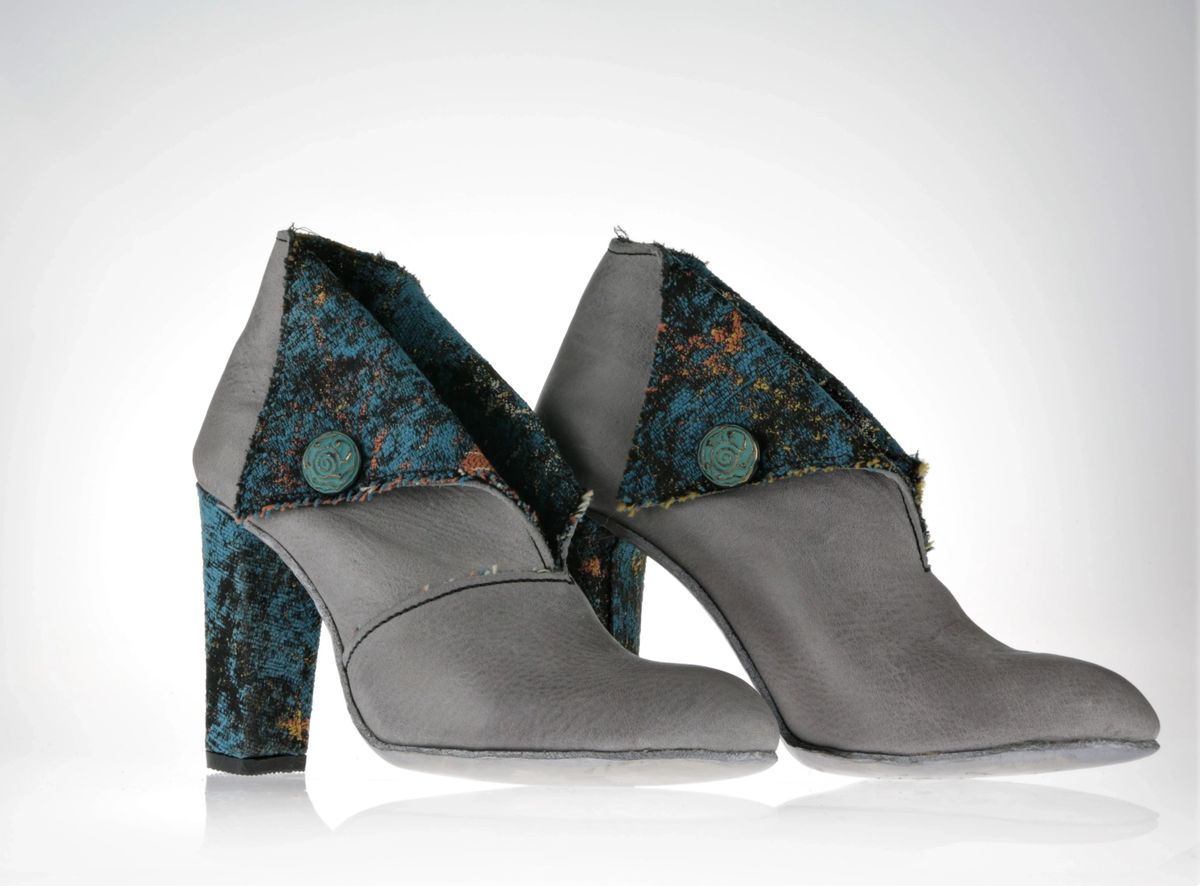 Boots in a combination of leather and fabric, with a dramatic opening on the front which takes away the need for zips or laces. Block 10 cm heel. Most of the upper is grey leather with the fabric as the lining. However, due to the dramatic opening the fabric folds over just like a shirt collar would do reveling it's blue hues with spots of gold and yellow. The fold is kept in place on each side by a button in oxidised copper, with a greenish hue. The heel is covered in the same fabric to add to the balance 